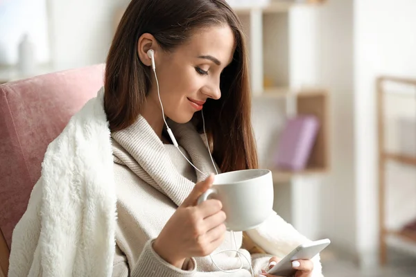 Beautiful young woman drinking tea while listening to music at home — Stock Photo, Image