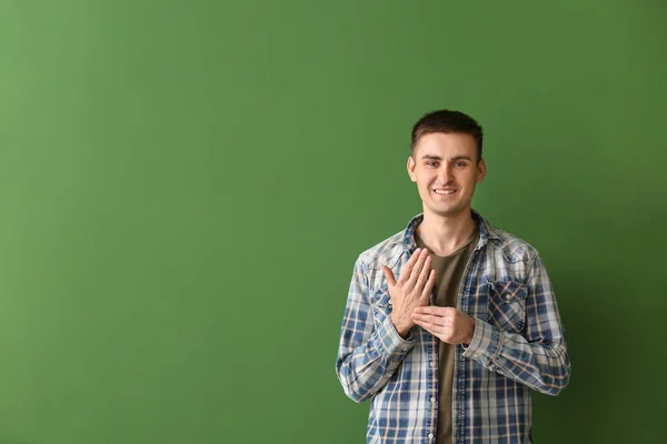 Young deaf mute man using sign language on color background — Stock Photo, Image