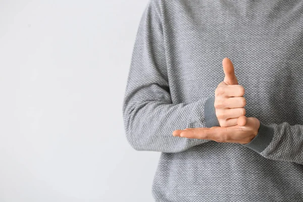 Young deaf mute man using sign language on light background — Stock Photo, Image