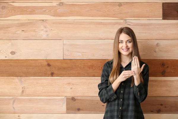 Young deaf mute woman using sign language on wooden background — Stock Photo, Image