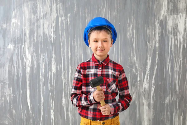 Симпатичный маленький мальчик в каске и с молотком на фоне гранжа — стоковое фото
