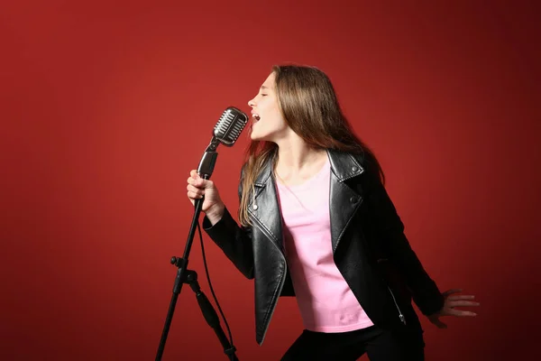 Teenage girl with microphone singing against color background — Stock Photo, Image