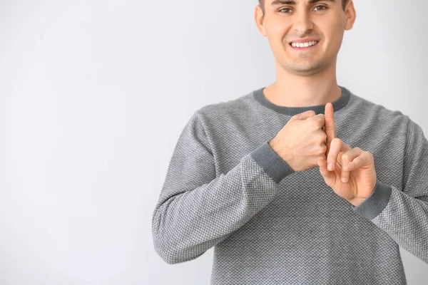 Joven hombre mudo sordo usando lenguaje de señas sobre fondo claro — Foto de Stock