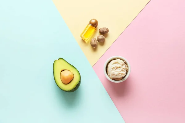 Bowl with shea butter, essential oil and avocado on color background