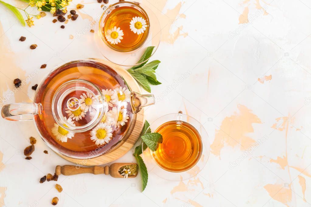 Teapot and cups of tasty chamomile drink on light background