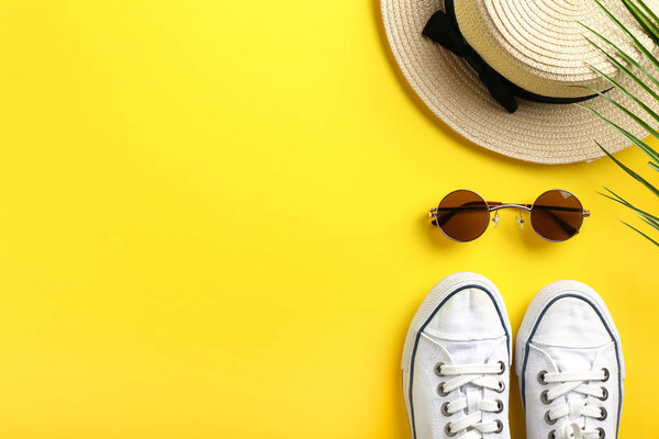 Stylish sunglasses with gumshoes and hat on color background