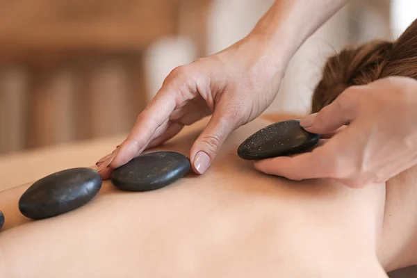 Schöne junge Frau in Behandlung mit Massagesteinen im Wellness-Salon — Stockfoto