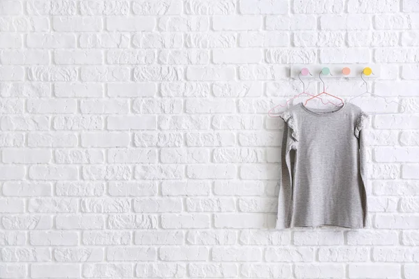 Hanger with child clothes on white brick wall — Stock Photo, Image