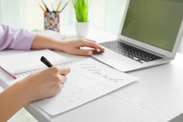Young woman marking date in calendar at table, closeup — Stock Photo, Image
