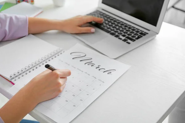 Young woman marking date in calendar at table, closeup — Stock Photo, Image