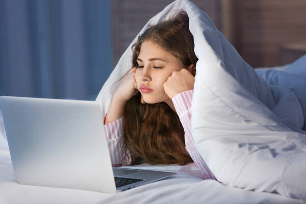 Teenage girl with laptop in bed at night