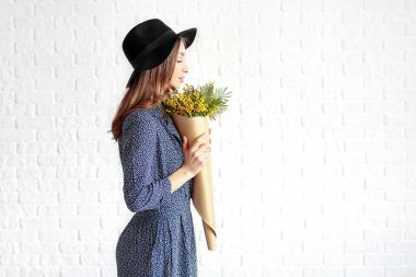Beyaz tuğla duvara karşı mimoza çiçek buketi ile güzel genç kadın