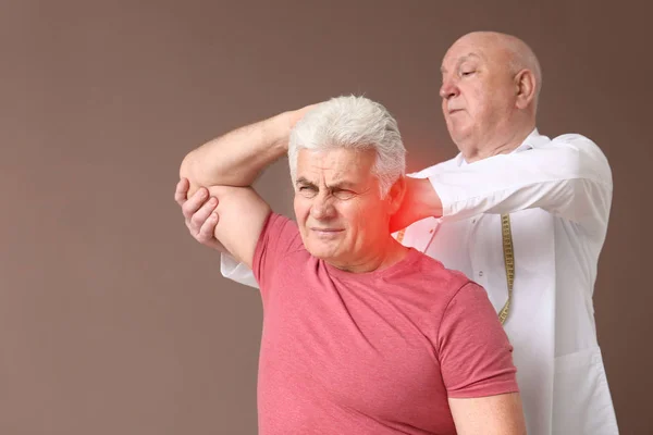 Seniorphysiotherapeut arbeitet mit reifem Mann an farbigem Hintergrund — Stockfoto