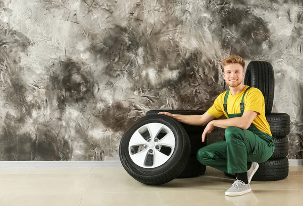 Young male mechanic with car tires near grunge wall — Stock Photo, Image