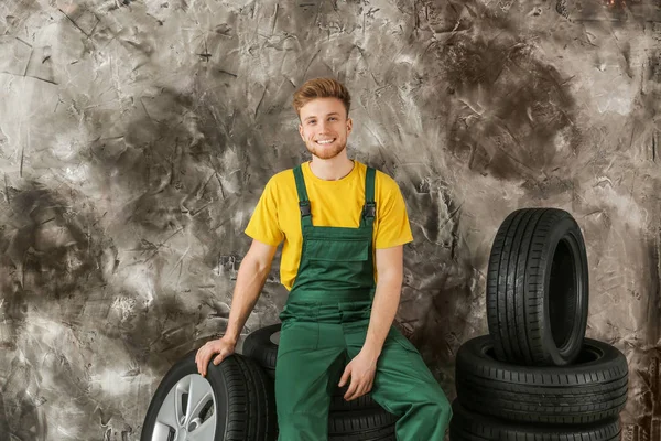 グランジの壁の近くに車のタイヤを持つ若い男性の整備士 — ストック写真