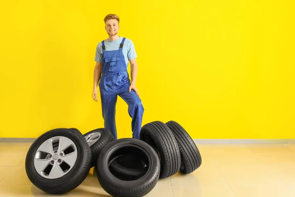 Jeune mécanicien masculin avec des pneus de voiture près du mur de couleur — Photo