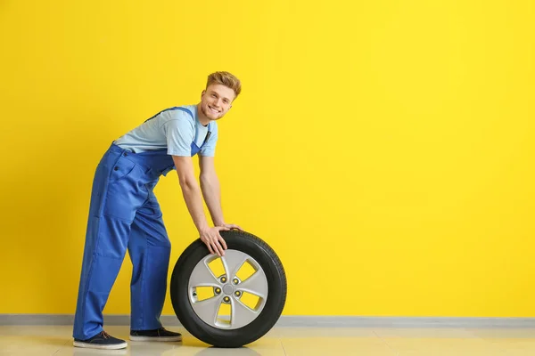 Young male mechanic with car tire near color wall — Stock Photo, Image