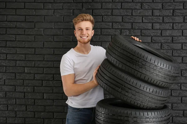 Young man with car tires against dark wall — Stock Photo, Image