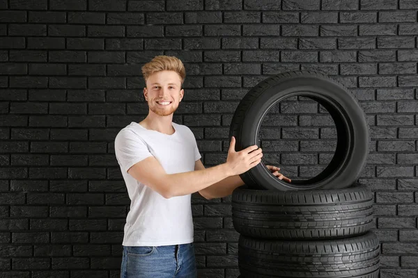 Jovem com pneus de carro contra parede escura — Fotografia de Stock