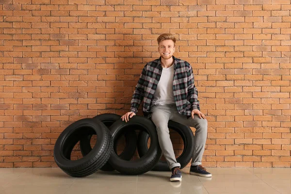 Молодий чоловік з автомобільними шинами біля цегляної стіни — стокове фото