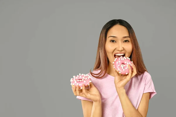 Asian woman with tasty donuts on grey background — Stock Photo, Image