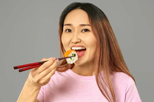 Азиатка ест вкусные суши на сером фоне — стоковое фото