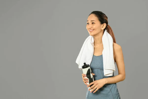 Αθλητική Ασιατική γυναίκα με μπουκάλι νερό σε γκρίζο φόντο — Φωτογραφία Αρχείου
