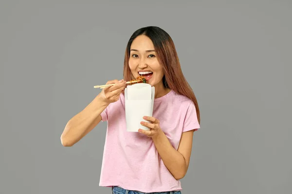 Aziatische vrouw eten Chinees eten op grijze achtergrond — Stockfoto