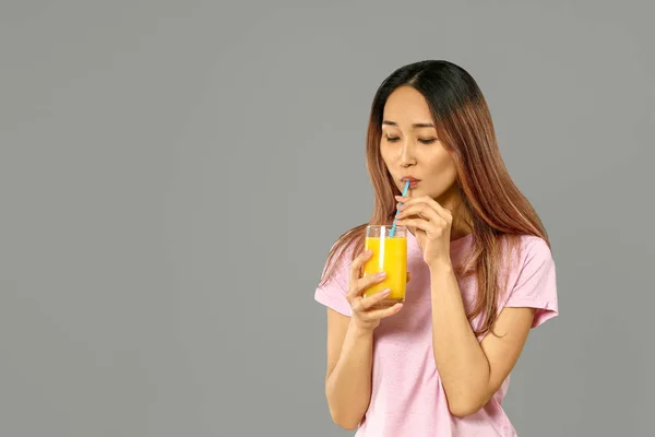 Femme asiatique avec verre de jus sur fond gris — Photo