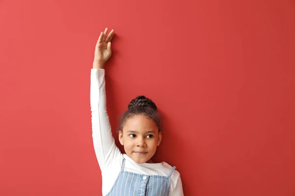 Cute African-American girl measuring height near color wall — Stock Photo, Image