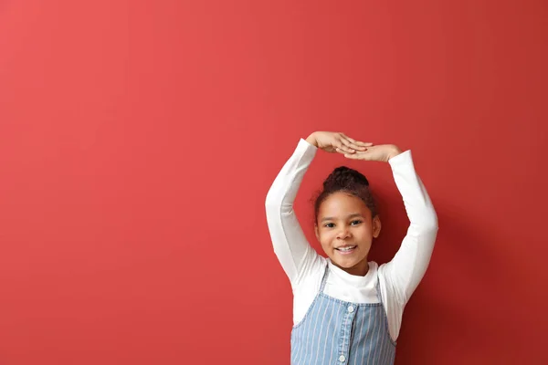 Cute African-American girl measuring height near color wall — Stock Photo, Image