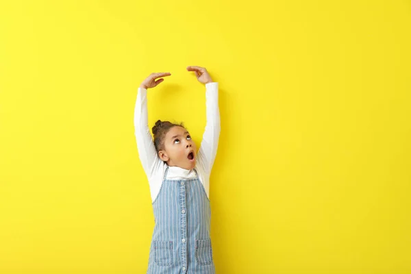 Cute little African-American girl measuring height near color wall — Stock Photo, Image