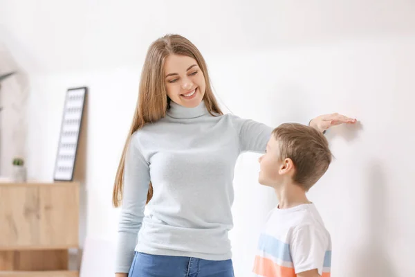 Mother measuring height of her son near wall — Stock Photo, Image