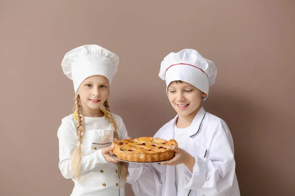 Cute little chefs with pie on color background — Stock Photo, Image