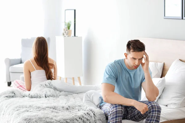 Upset young man after quarrel with wife sitting on bed — Stock Photo, Image