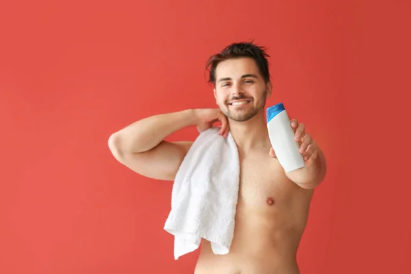 Hombre guapo con botella de champú y toalla sobre fondo de color — Foto de Stock