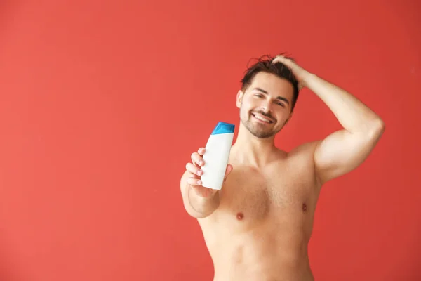 Handsome man with bottle of shampoo on color background — Stock Photo, Image