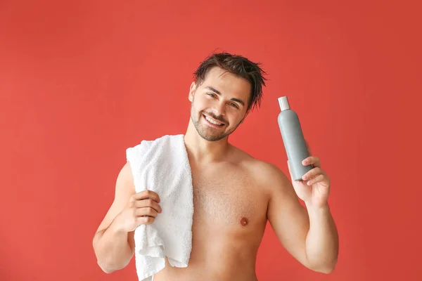 Homem bonito com garrafa de xampu e toalha no fundo de cor — Fotografia de Stock