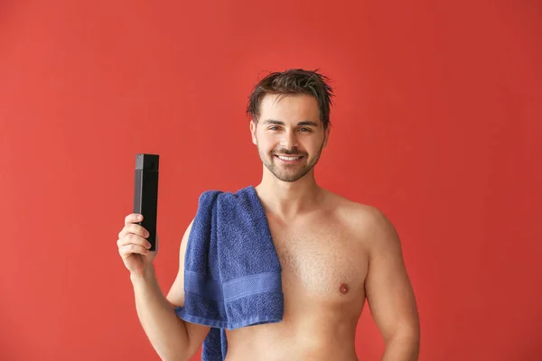 Handsome man with bottle of shampoo and towel on color background — Stock Photo, Image