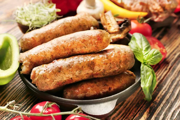 Frying pan with tasty grilled sausages on wooden table — Stock Photo, Image