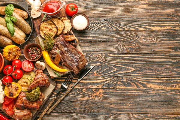 Смачне м'ясо на грилі з ковбасками та овочами на дерев'яному фоні — стокове фото