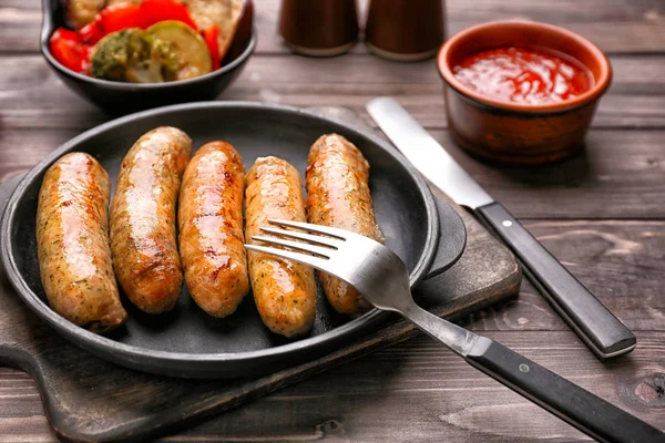 Frying pan with tasty grilled sausages on wooden table — Stock Photo, Image