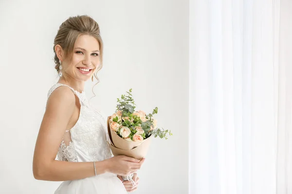 Mooie jonge bruid met boeket van bloemen in de buurt van venster — Stockfoto