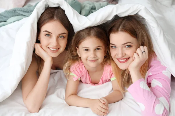 Happy lesbian couple with little daughter lying under blanket in bed — Stock Photo, Image