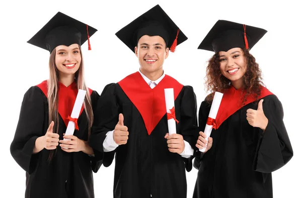 Jovens estudantes em vestes de solteiro mostrando polegar-up no fundo branco — Fotografia de Stock