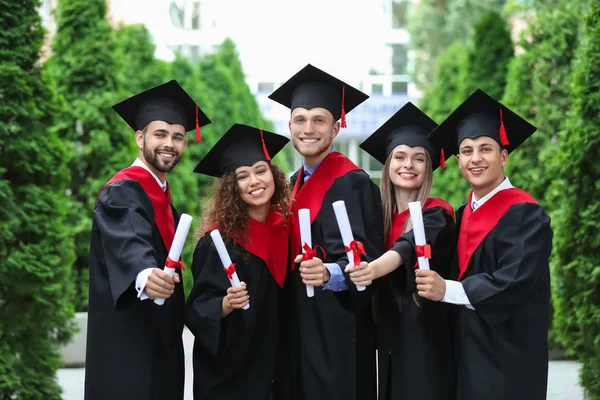 Šťastní studenti ve bakalářských róbách a s diplomy venku — Stock fotografie