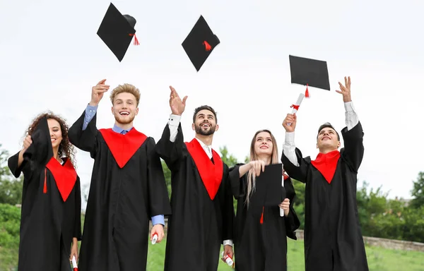 Allievi felici in abiti da scapolo gettando cappelli laurea all'aperto — Foto Stock