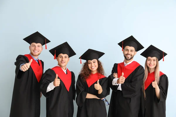 Молоді студенти в холостяцькому одязі показують великий палець на кольоровому фоні — стокове фото