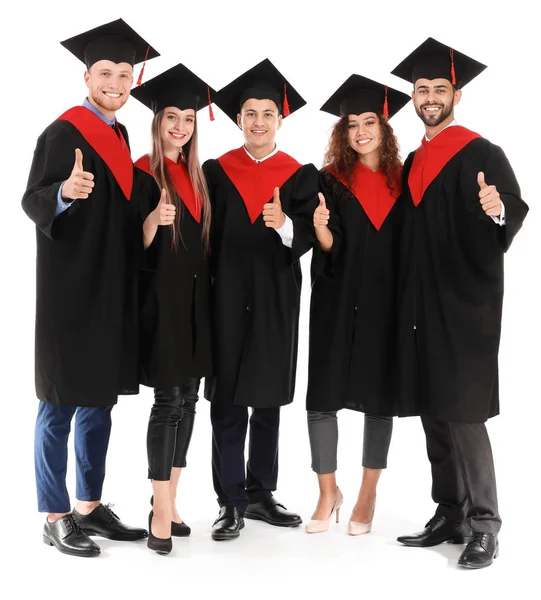 Jovens estudantes em vestes de solteiro mostrando polegar-up no fundo branco — Fotografia de Stock