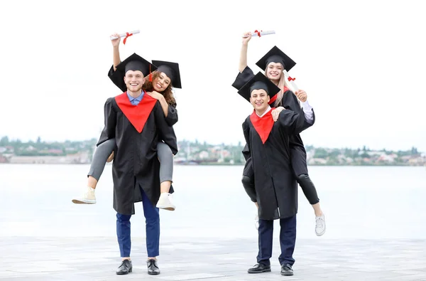 Happy students in bachelor robes and with diplomas outdoors